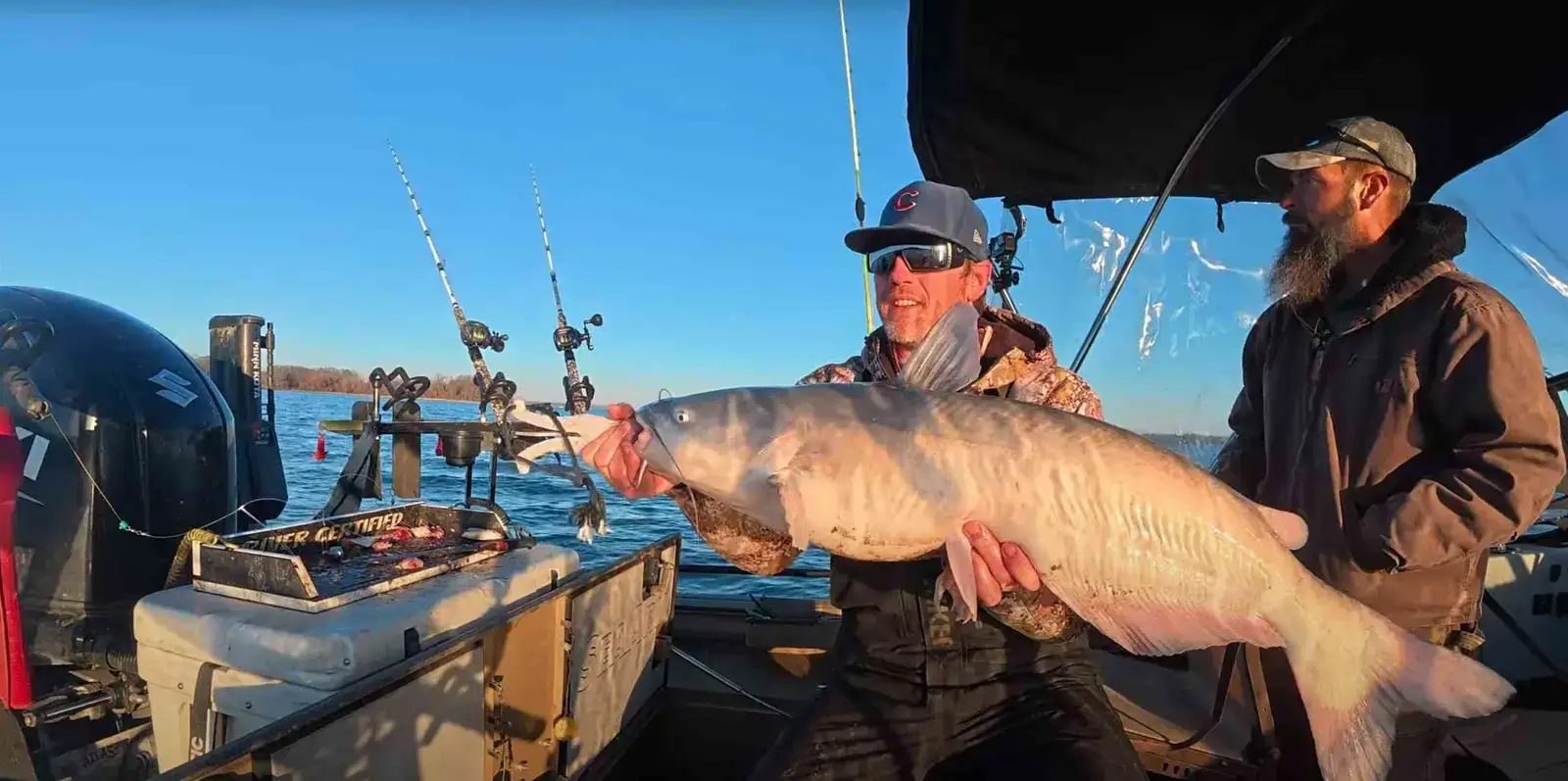 Spencer Bauer holds up a hefty blue catfish aboard his boat on a sunny winter day.